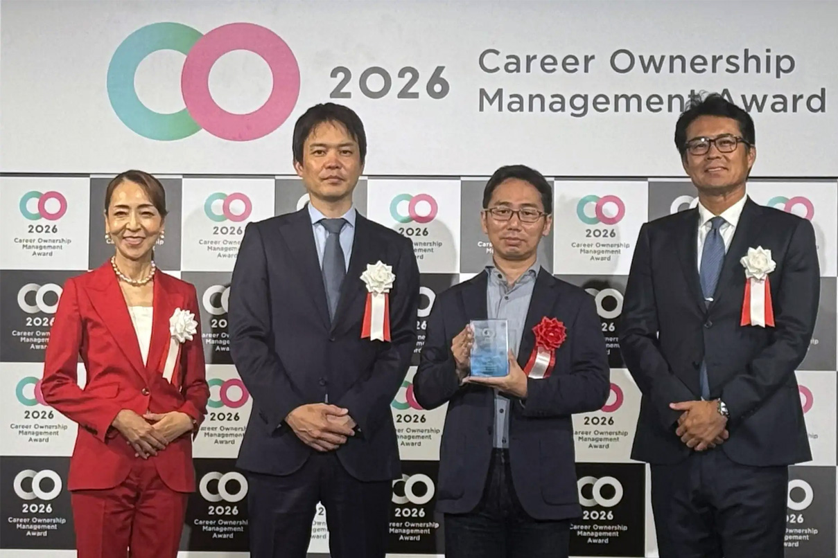 Group of four professionally dressed individuals posing at an award ceremony with a '2026 Career Ownership Management Award' backdrop and ribbons on their outfits.