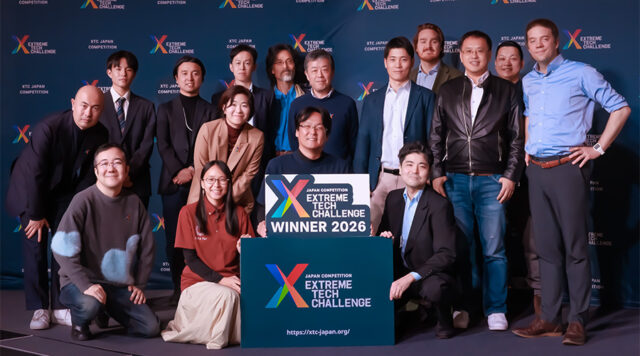 Group photo of winners and teammates on stage with an Extreme Tech Challenge 2026 sign backdrop and banner walls in the background.