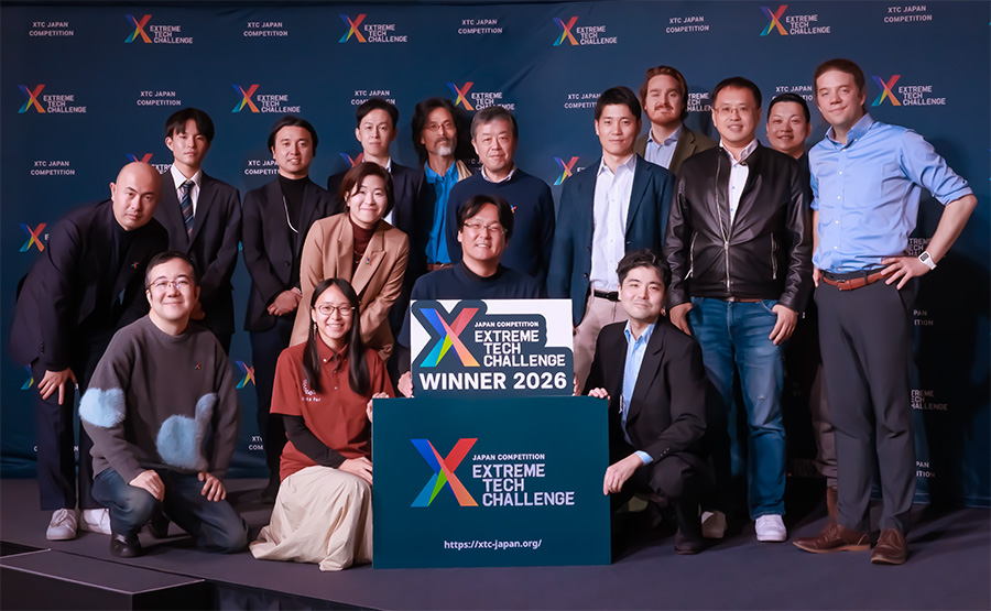 Group photo of winners and teammates on stage with an Extreme Tech Challenge 2026 sign backdrop and banner walls in the background.