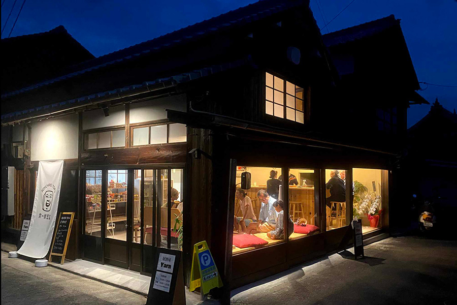Night view of a traditional wooden Japanese storefront with warm interior lighting and people dining inside. (Informative)