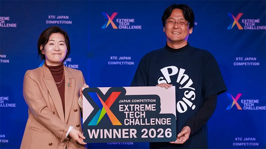 Two people pose with a large winner sign reading 'Extreme Tech Challenge 2026' in front of a blue event backdrop showing the logo.