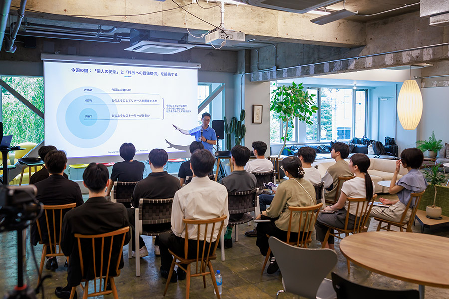 Instructor giving a presentation to about 20 people in a bright, modern coworking space with a slide showing circular diagrams on screen