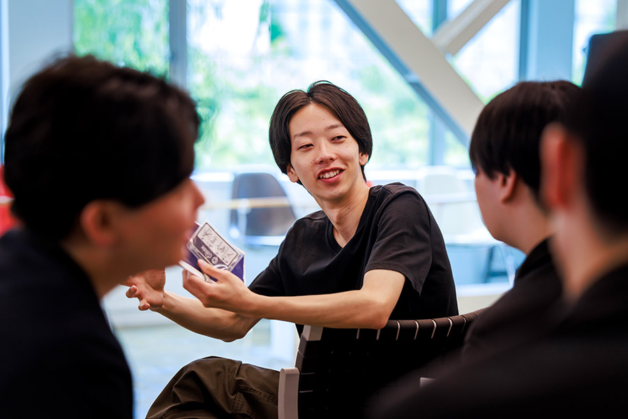 Young man in a black shirt shares a card with teammates during a casual group discussion in a bright room.