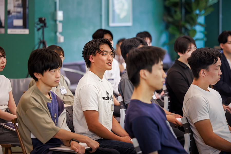 Group of young adults seated in a classroom or conference room, listening attentively to a speaker.
